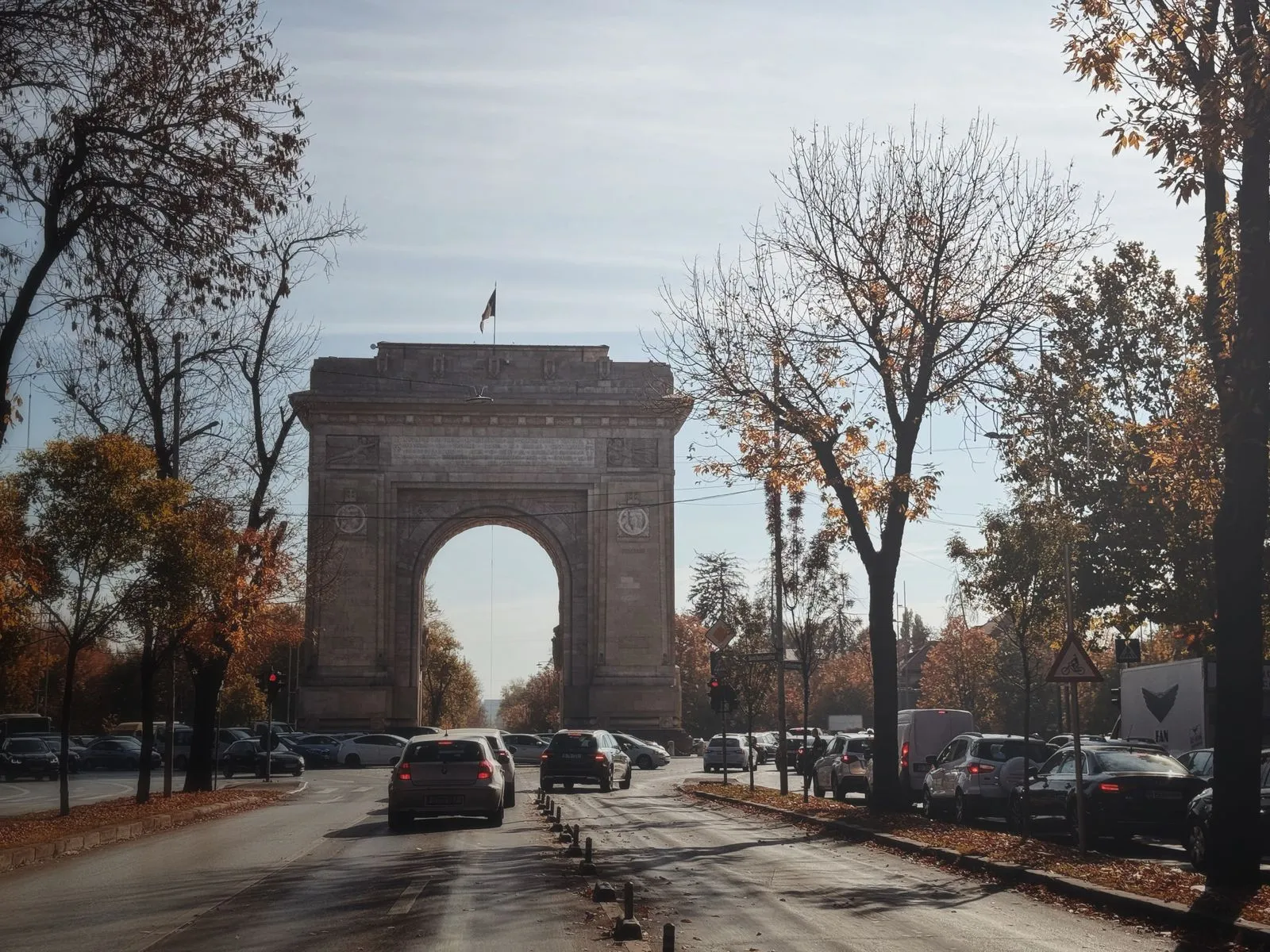 Arcul de Triumf din București toamna, înconjurat de copaci galbeni și trafic