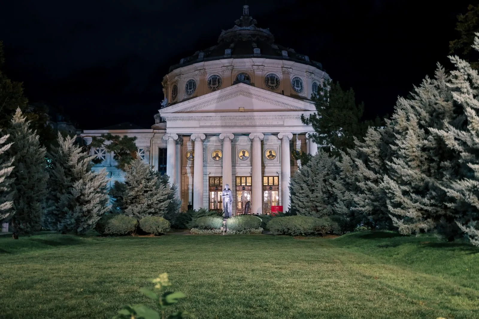 Ateneul Român luminat noaptea, iarna, cu brazi în față, în centrul Bucureștiului