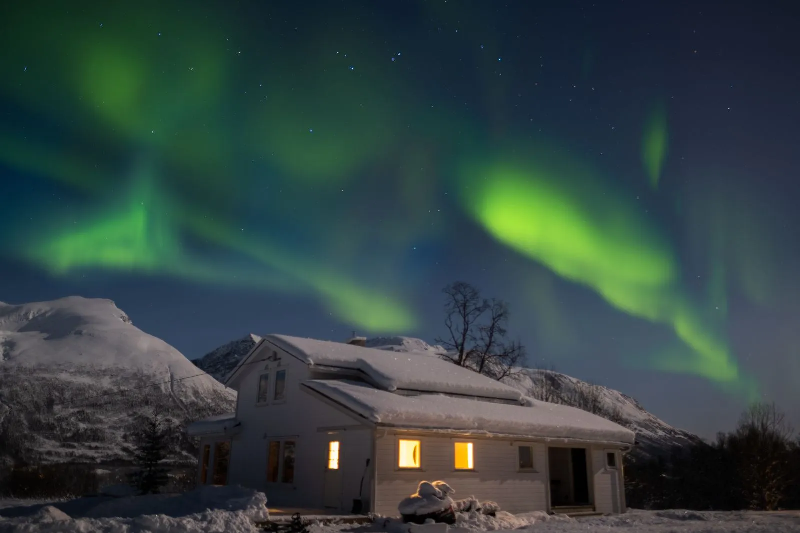 Aurora verde deasupra unei case acoperite de zăpadă, lângă Tromsø, Norvegia