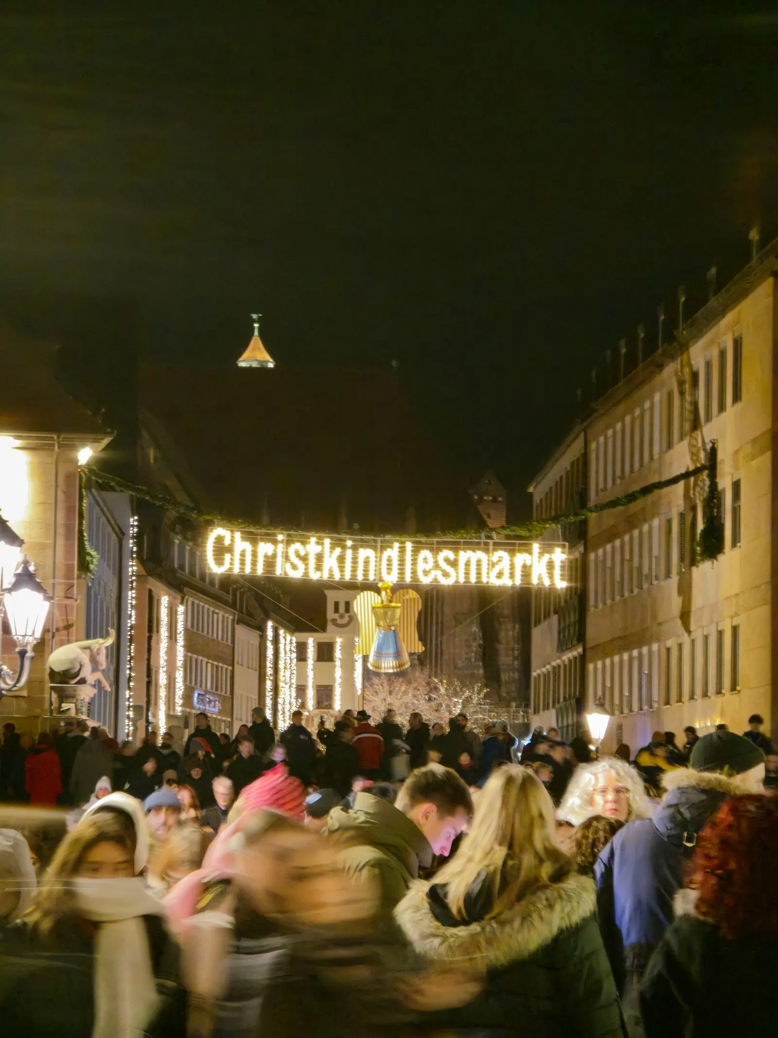 Mulțime seara sub inscripția luminată Christkindlesmarkt, la intrarea în târgul din Nürnberg