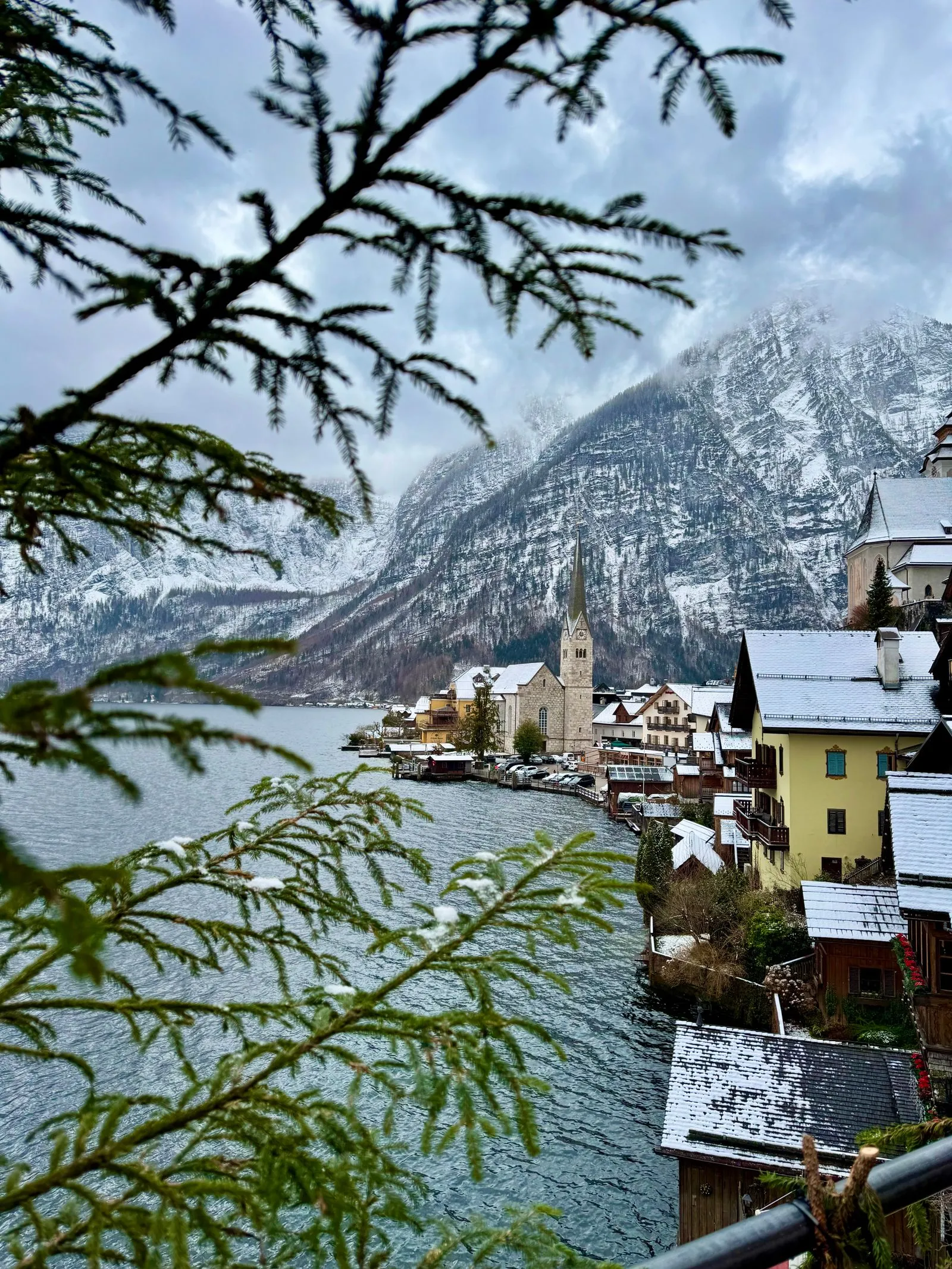 Hallstatt iarna, cu case acoperite de zăpadă pe malul lacului și biserica din sat
