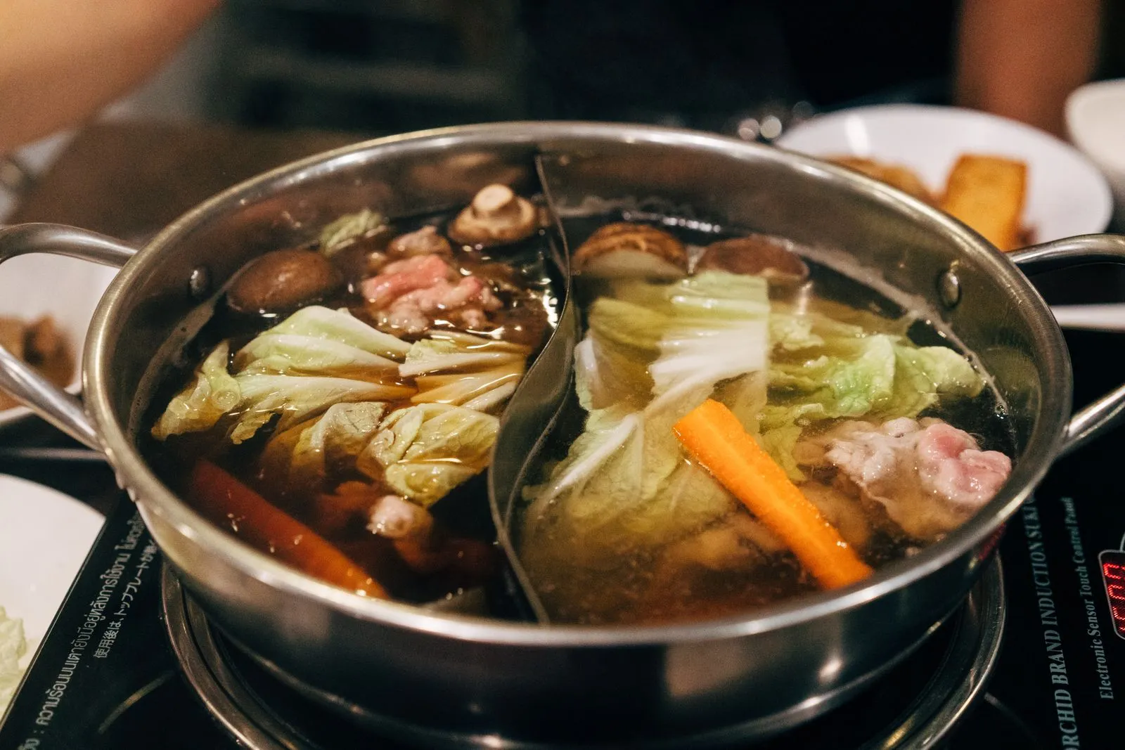 Hot pot chinezesc cu două supe, carne feliată, varză chinezească și ciuperci, pe plită la masă