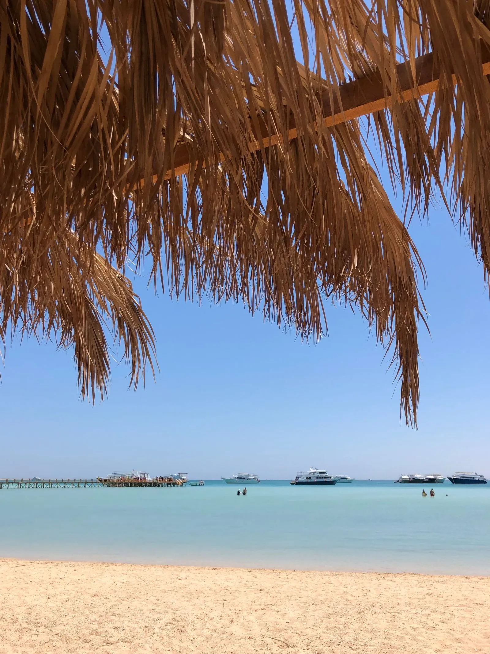 Plajă cu apă turcoaz și umbrele din frunze de palmier la Hurghada, pe Marea Roșie