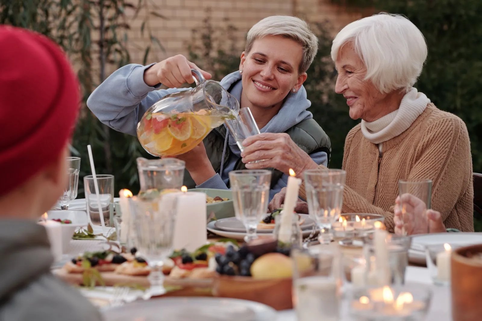 O femeie toarnă limonadă bunicii la o masă festivă în grădină, seara, cu lumânări aprinse pe masă