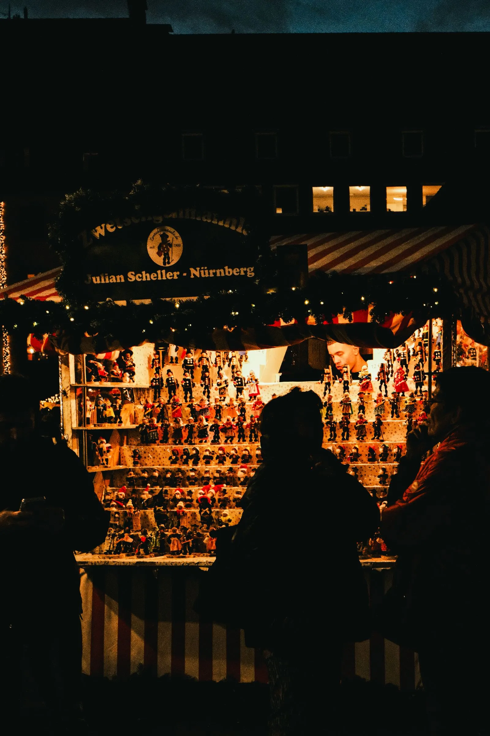 Căsuță de târg din Nürnberg cu figurine și decorațiuni de Crăciun, luminată seara