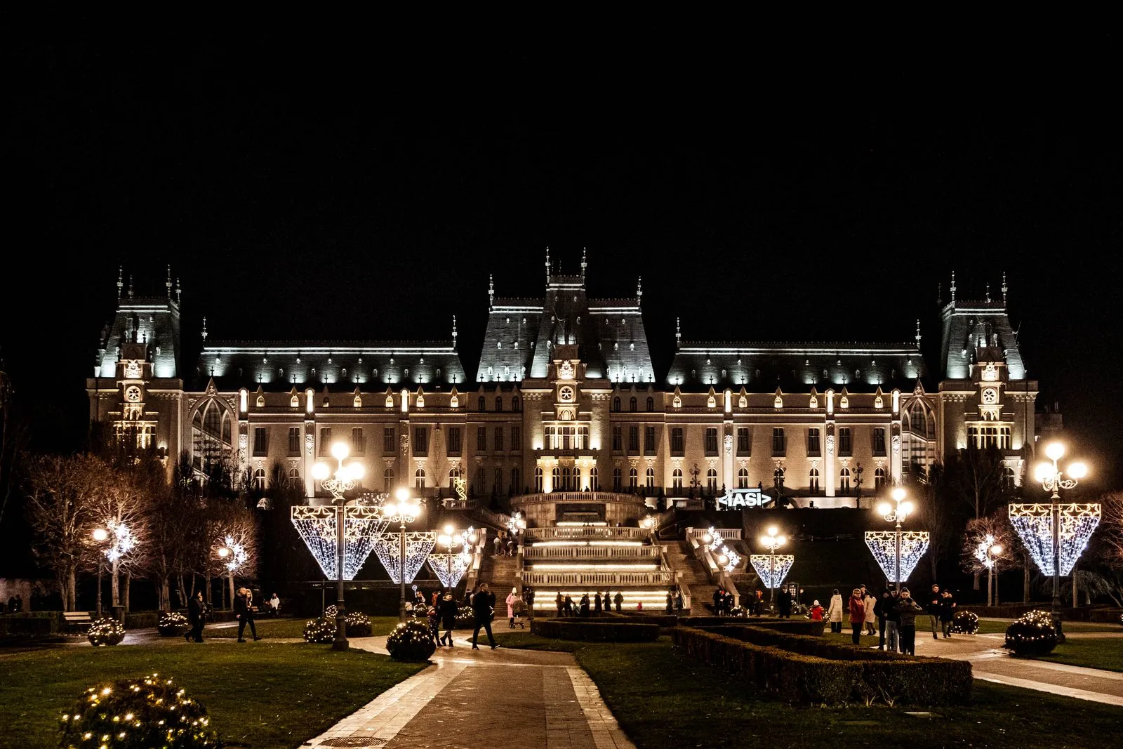 Palatul Culturii din Iași luminat noaptea, cu instalațiile de sărbători din parcul din față