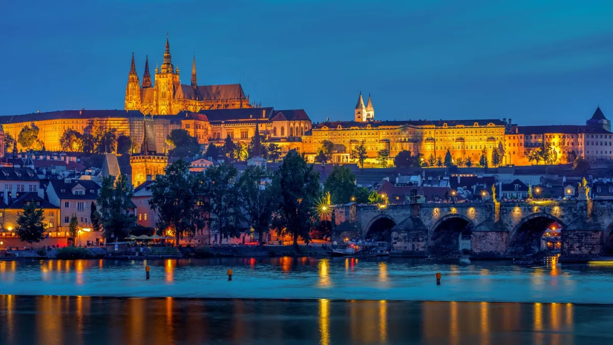 Castelul din Praga și Podul Carol iluminate, reflectate în Vltava la căderea nopții