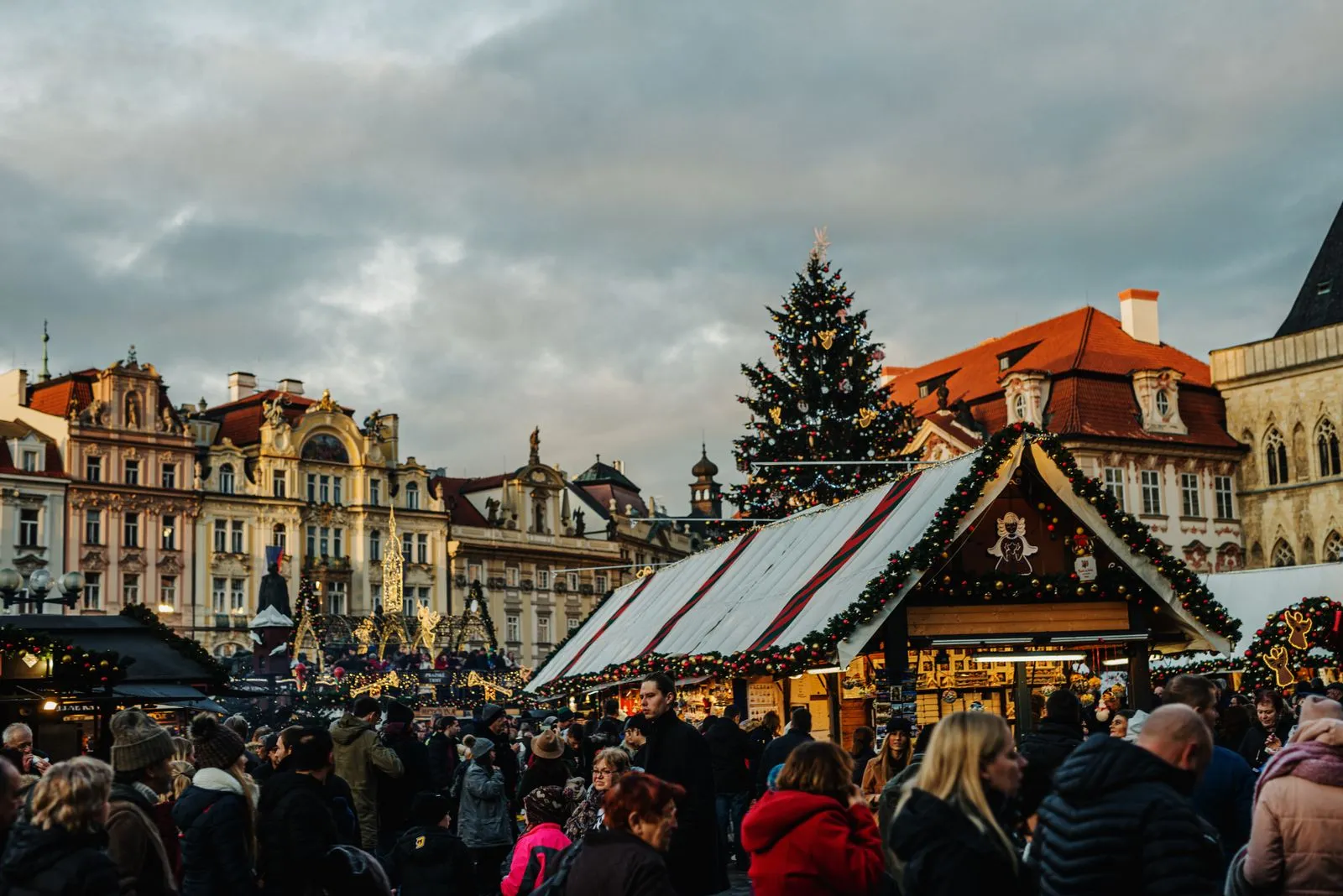Căsuțele târgului de Crăciun și bradul din Piața Orașului Vechi din Praga, cu vizitatori printre standuri
