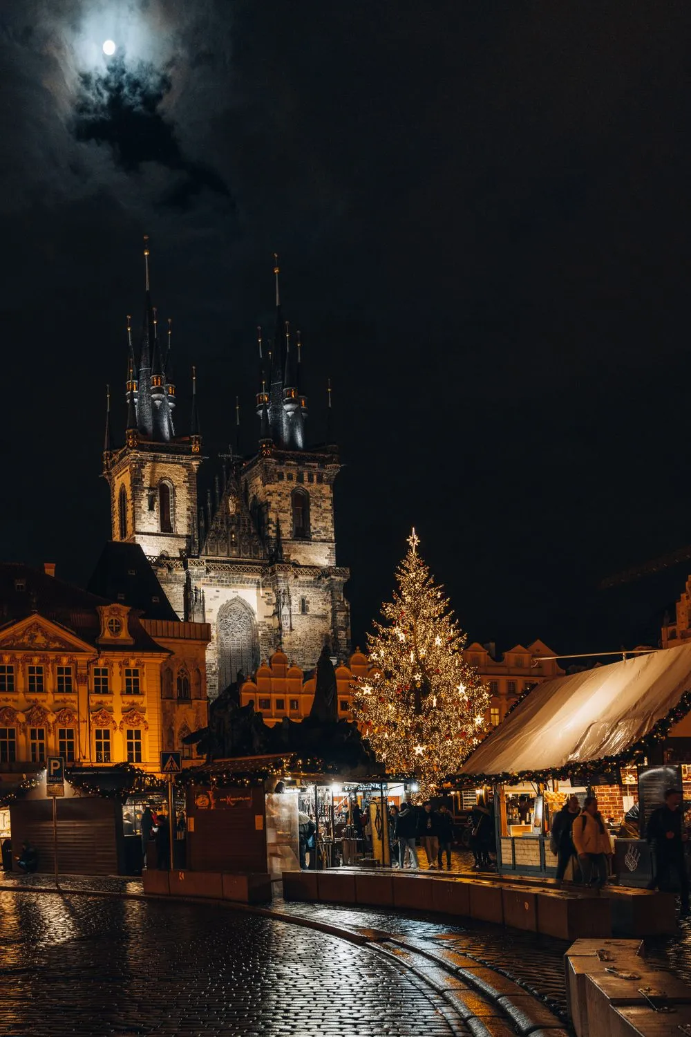 Bradul de Crăciun și căsuțele târgului din Piața Orașului Vechi din Praga noaptea, cu Biserica Týn luminată în spate
