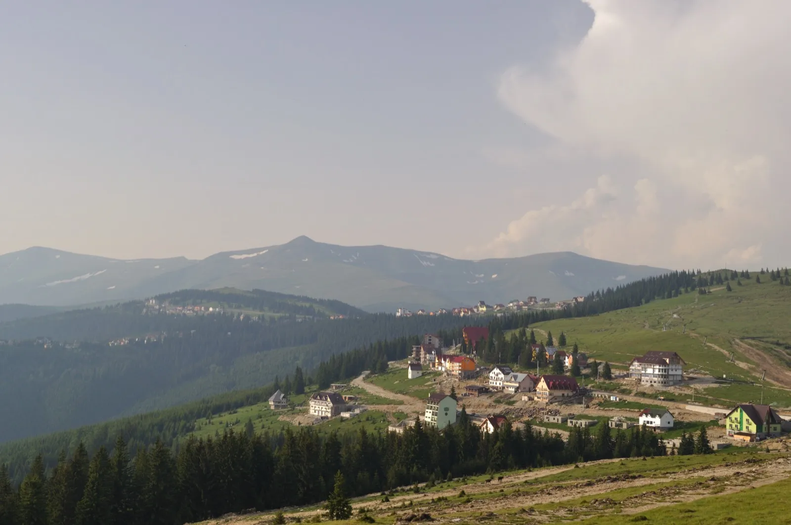 Rânca văzută de pe DN67C, cu pensiunile pe platou și serpentinele drumului
