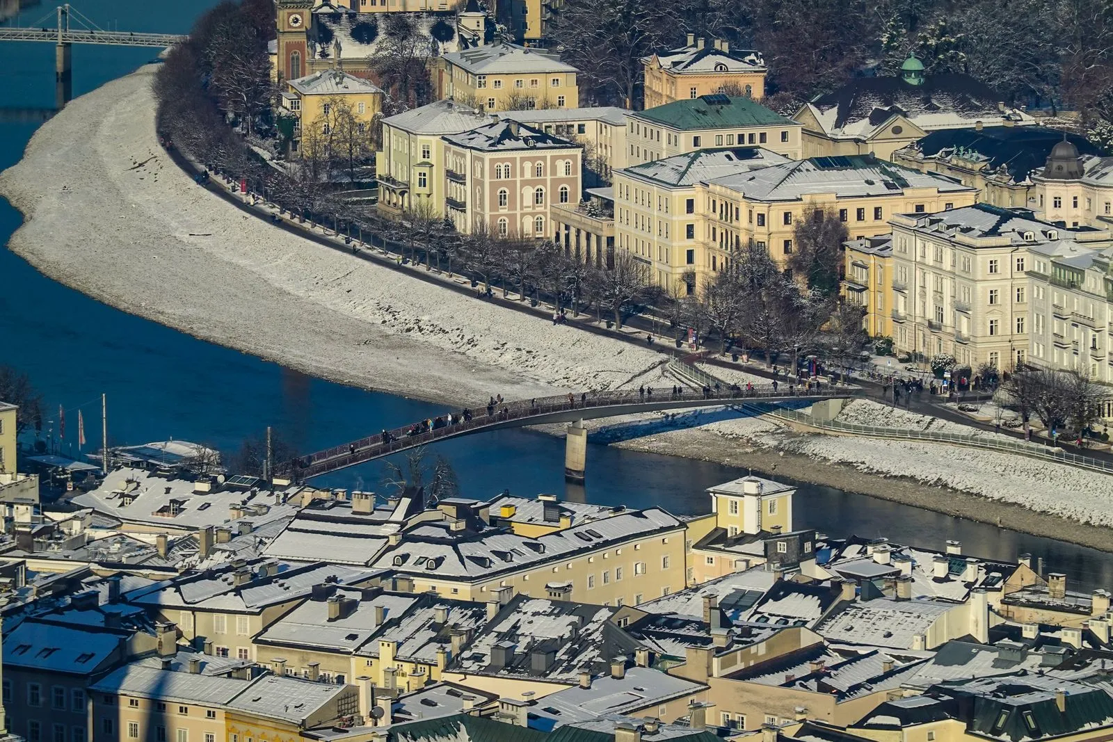 Salzburg iarna, cu acoperișuri acoperite de zăpadă și pasarela peste râul Salzach
