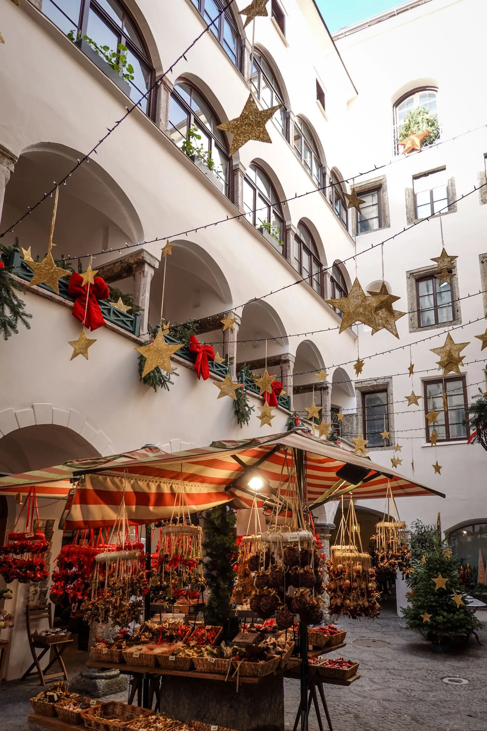 Tarabă cu decorațiuni de Crăciun într-o curte cu arcade din centrul vechi al Salzburgului, sub stele aurii