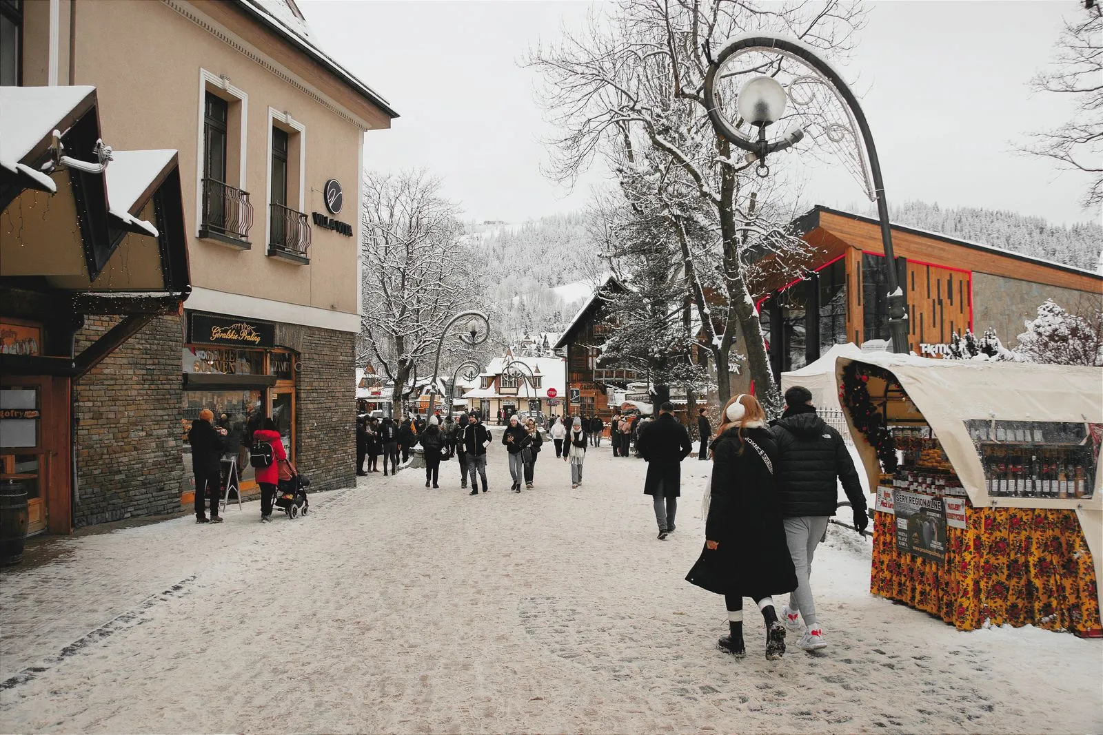 Strada Krupówki din Zakopane iarna, cu zăpadă, trecători și o tarabă cu brânză oscypek