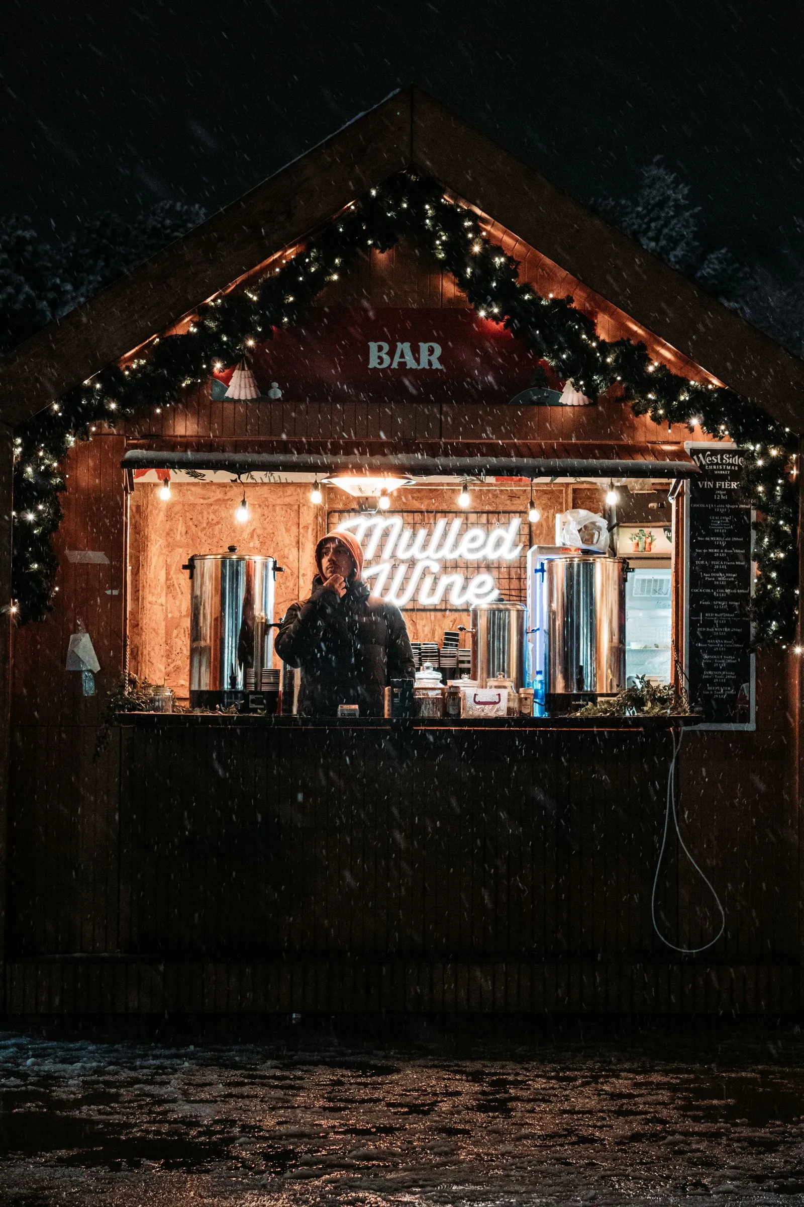Căsuță de vin fiert decorată cu ghirlande la un târg de Crăciun din București, noaptea