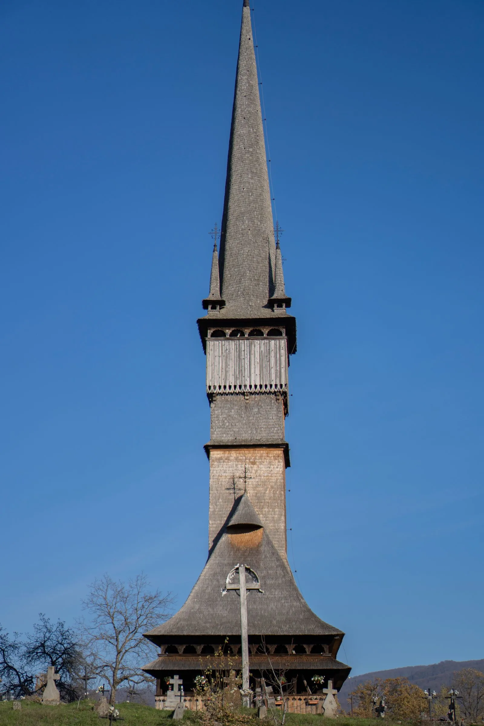 Turnul bisericii de lemn din Șurdești, Maramureș, cu acoperiș de șindrilă și cruci de lemn în cimitir