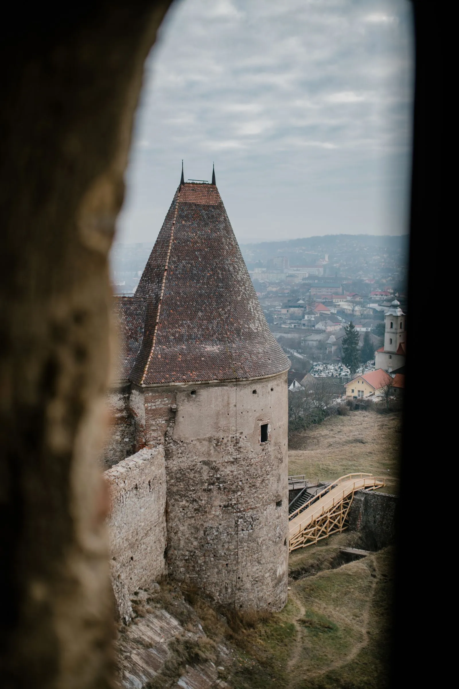 Un turn al castelului văzut printr-o fereastră, cu orașul Hunedoara în fundal