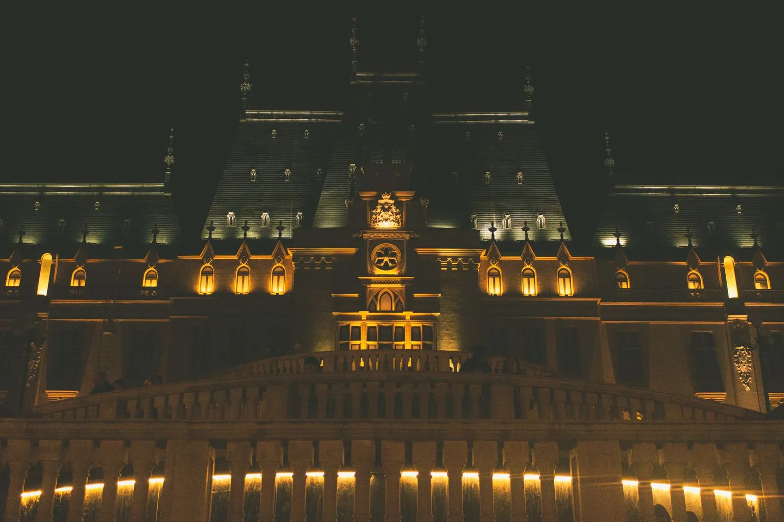 Fațada Palatului Culturii din Iași luminată noaptea, cu ceasul și stema deasupra intrării