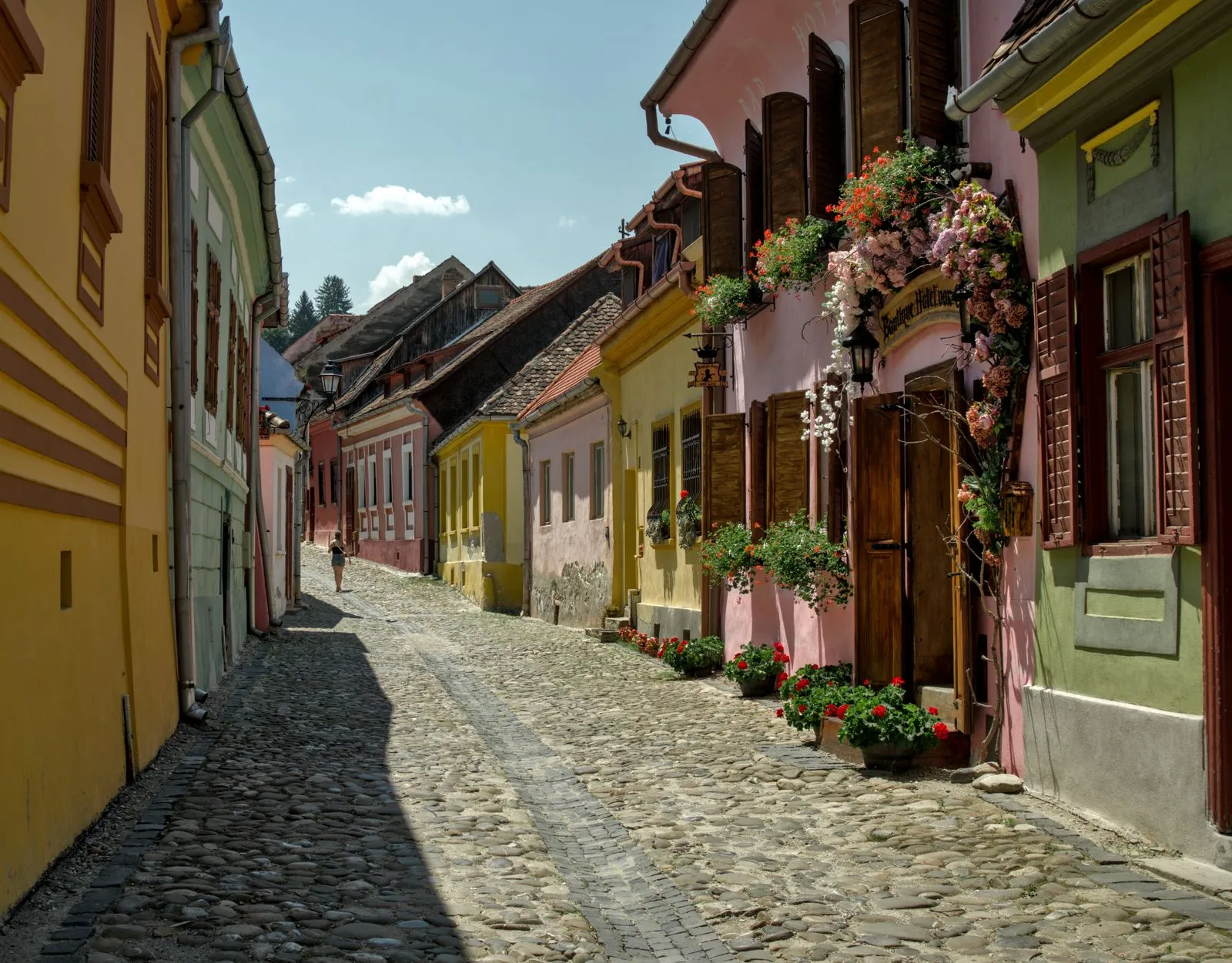 Stradă pavată cu case colorate și flori la ferestre în Cetatea Sighișoara